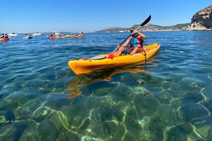 A person kayaking on clear water with a rocky coastline in the background. 3