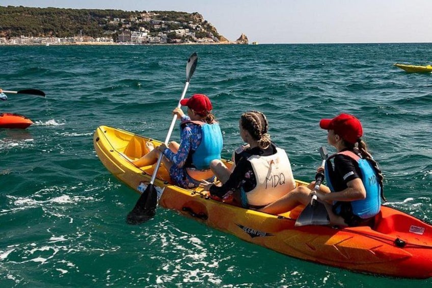 Three people kayaking on a calm sea with a coastal landscape in the background. 2