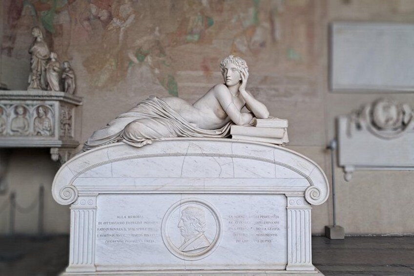 A marble statue of a reclining woman with a book, set on a pedestal with inscriptions. 4