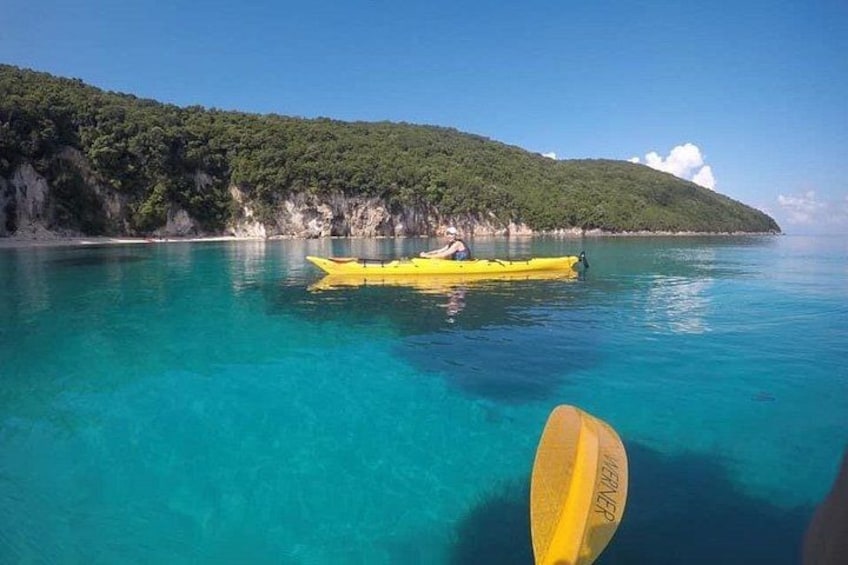 A clear turquoise sea, a yellow kayak, and a green hill with dense vegetation. 1