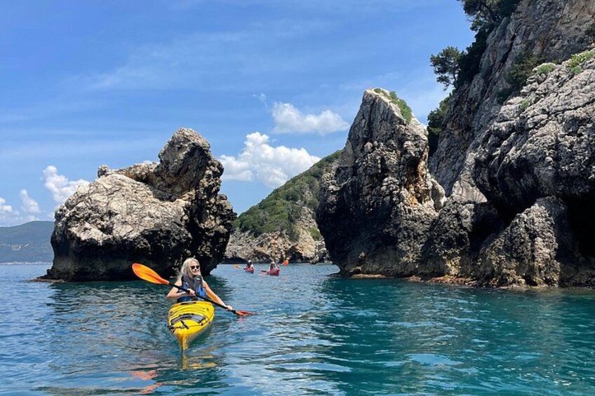 A kayaker in a clear blue sea with rocky cliffs and other kayakers in the background. 3