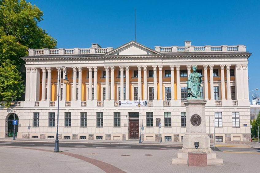 Un grand bâtiment de style néoclassique, orné de colonnes et d’une statue, se dressant sous un ciel d’un bleu limpide. 2