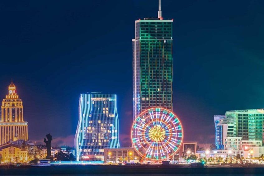 Un orizzonte cittadino notturno con edifici illuminati, una ruota panoramica e un edificio storico. 1