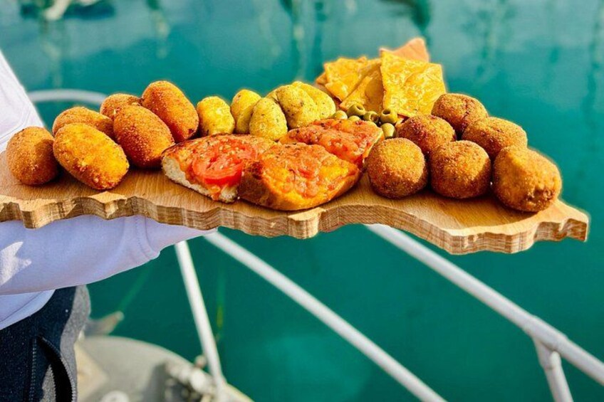En træbakke med forskellige friturestegte retter, herunder croquettes og en skive tomat. 3