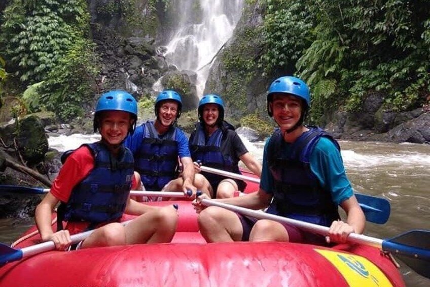 A group of people in a red inflatable raft on a river with a waterfall in the background. 5
