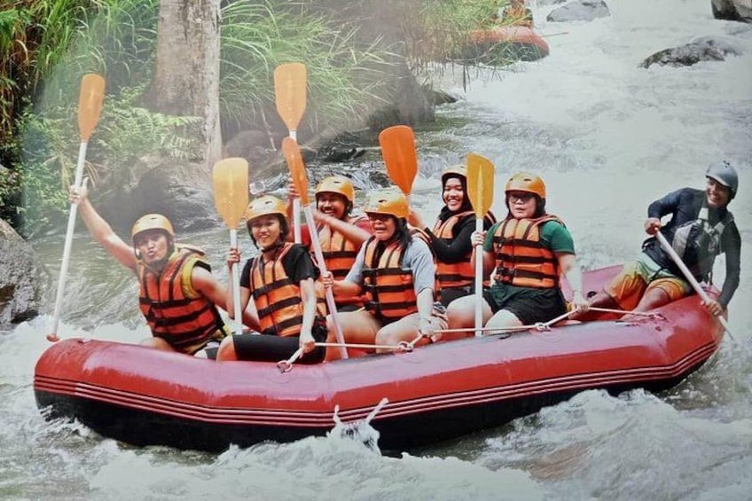 A group of people in a red inflatable raft on a river, wearing life jackets and helmets. 5