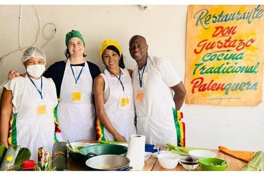 Cuatro personas con delantales y mascarillas faciales, de pie en una cocina con utensilios de cocina e ingredientes. 4
