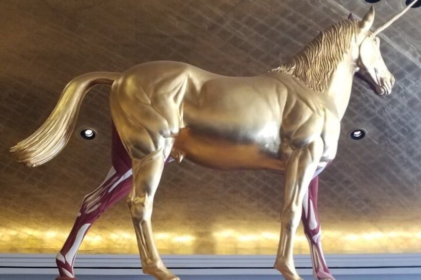 A golden horse statue with a long tail and a mane, standing on a platform. 5