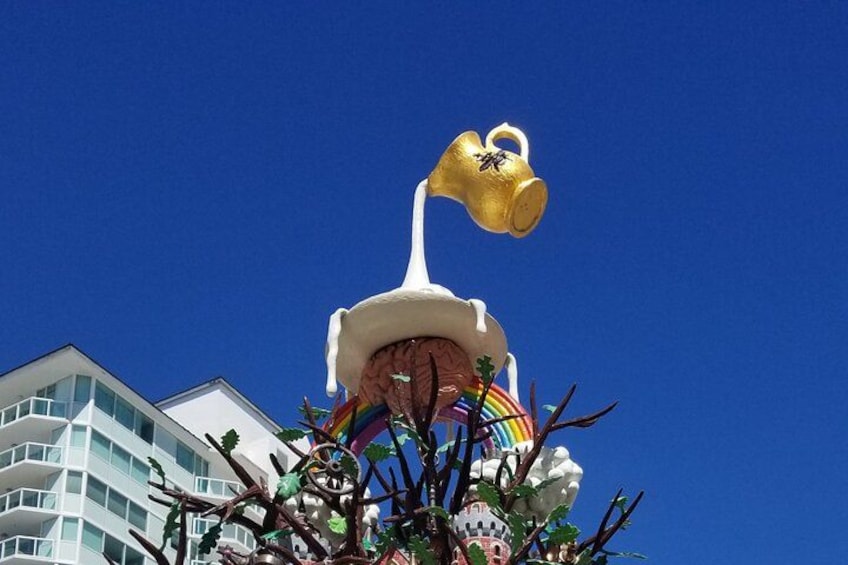 A large golden watering can sculpture with a rainbow and a castle-like structure. 3