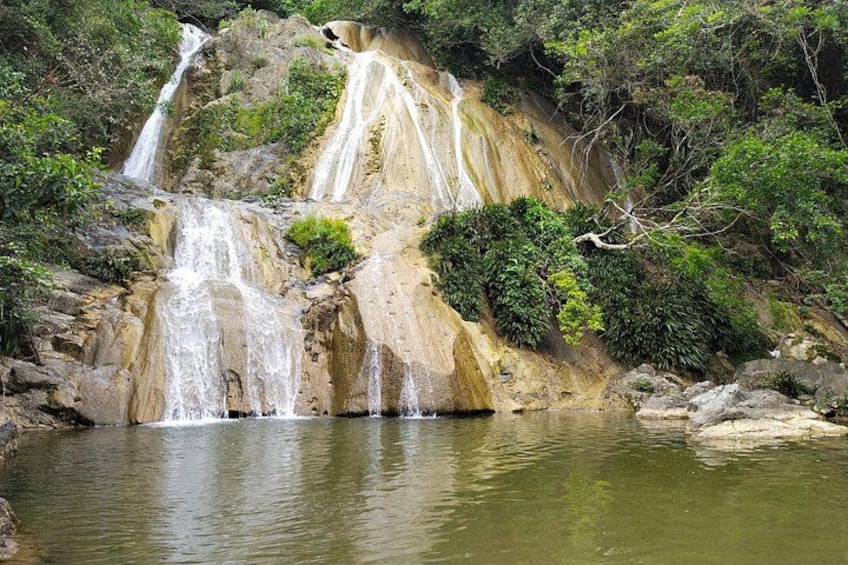 Une cascade d’eau se précipite le long d’une falaise rocheuse pour se déverser dans un bassin paisible, entouré d’une végétation luxuriante. 2