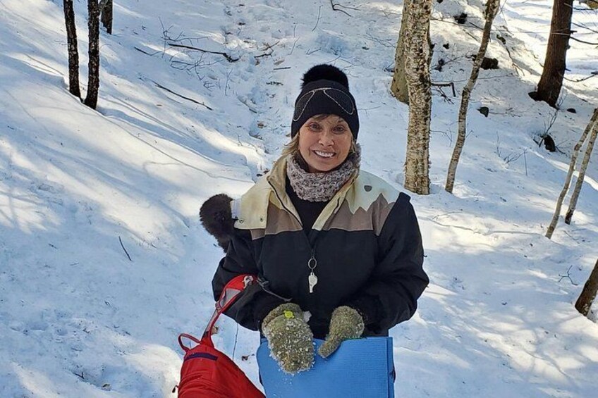 A person in a snowy forest with bare trees, holding a red bag. 3