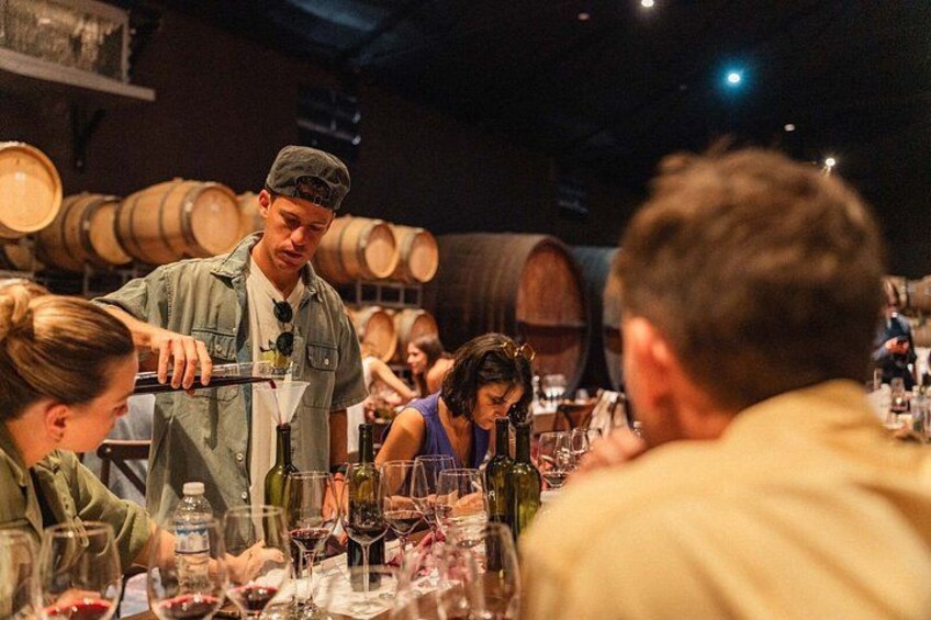 A person pouring wine into glasses at a restaurant with patrons seated at tables. 2
