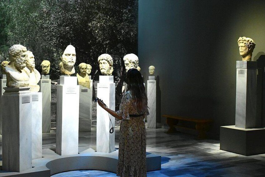 A museum exhibit with busts on pedestals, a person observing, and a bench in the background. 2