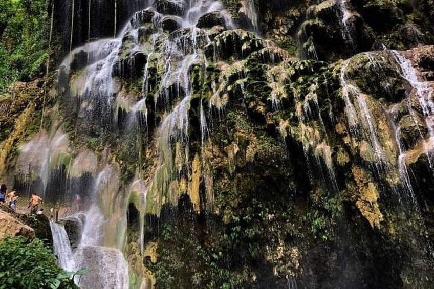 A multi-tiered waterfall cascading over moss-covered rocks in a forested area. 3