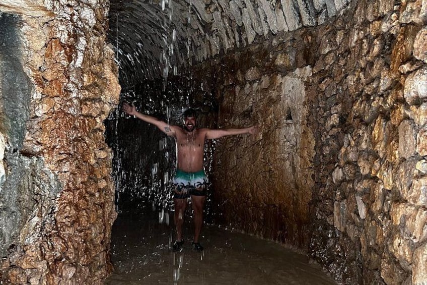 A person standing in a cave with water falling from above. 4