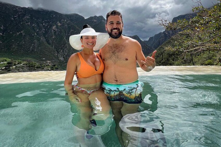 Two people in a clear blue pool with mountains in the background. 5