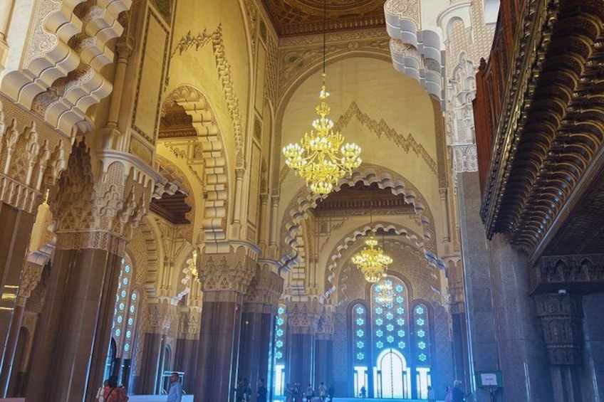 An interior of a grand building with intricate arches, columns, and a large chandelier. 2