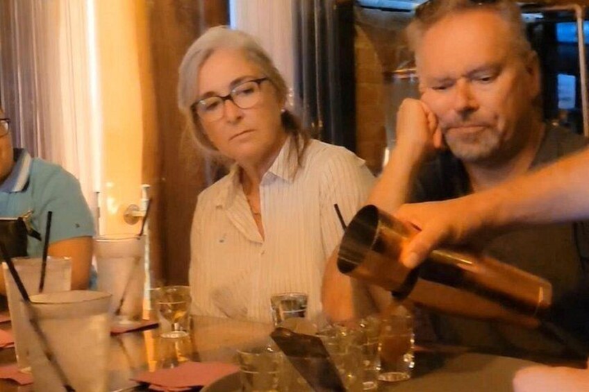 Une personne verse une boisson dans un verre sur une table où sont assis d’autres convives. 3