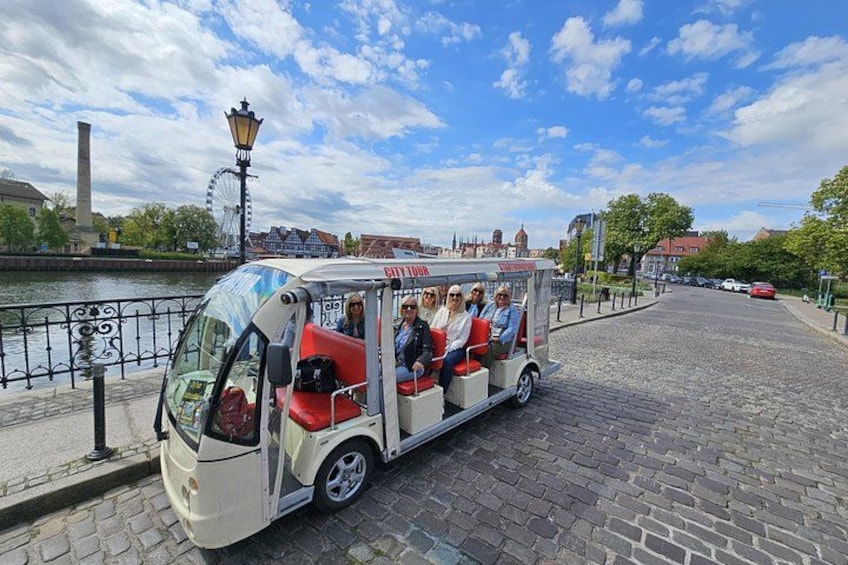 A narrowboat with passengers on a cobblestone street near a river. 4