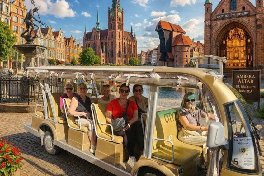 En gruppe mennesker på sightseeingtur i en historisk bymidte med markant arkitektur og en flod. 4
