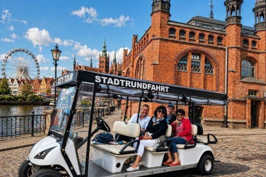 En turistbus med passagerer foran en historisk bygning med et tårn og et ur. 1