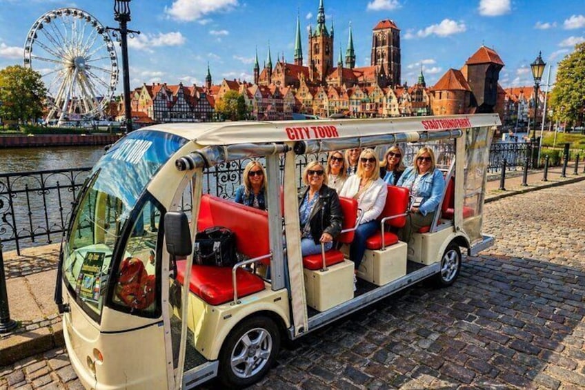 En turistbus med passagerer, et pariserhjul og historiske bygninger i baggrunden. 3