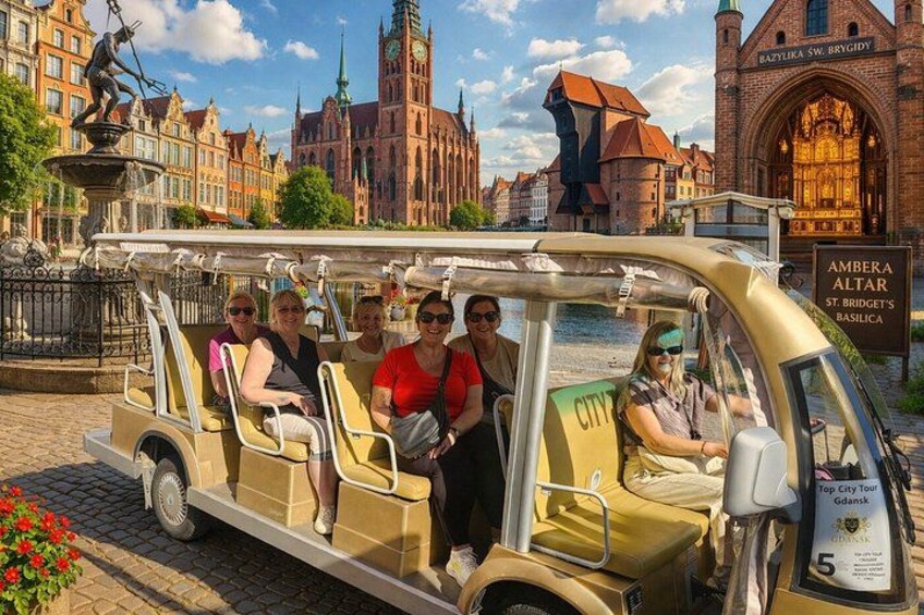 A group of people on a city tour vehicle in a historic European city with notable architecture and a river. 2