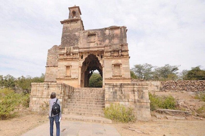 A historical stone structure with an arched entrance, a person standing in front, and a clear sky. 3