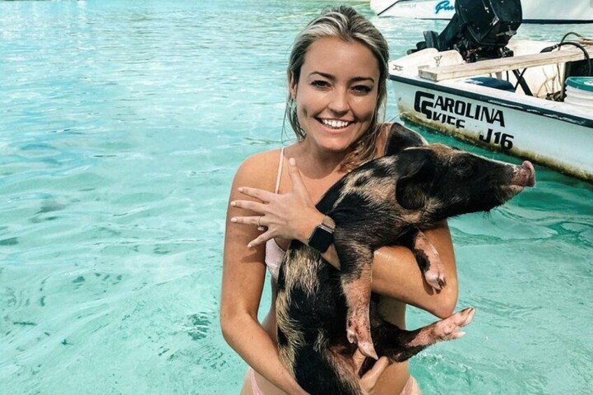 A person holding a piglet in clear blue water with a boat in the background. 5
