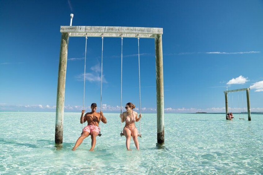 Two people swinging on a wooden swing over clear turquoise water. 1