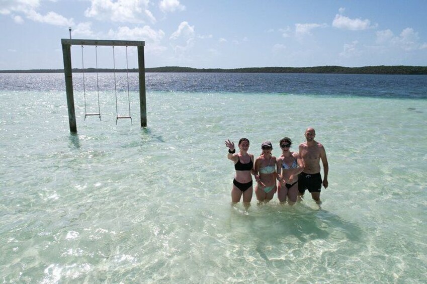 A group of people in clear turquoise water with a swing set in the background. 3