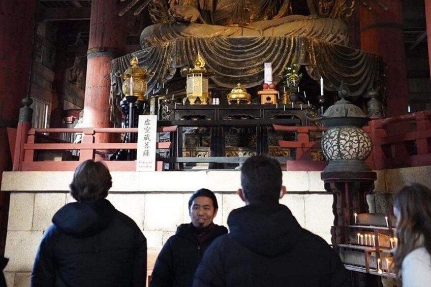 A group of people in a temple with a large statue and ornate decorations. 2
