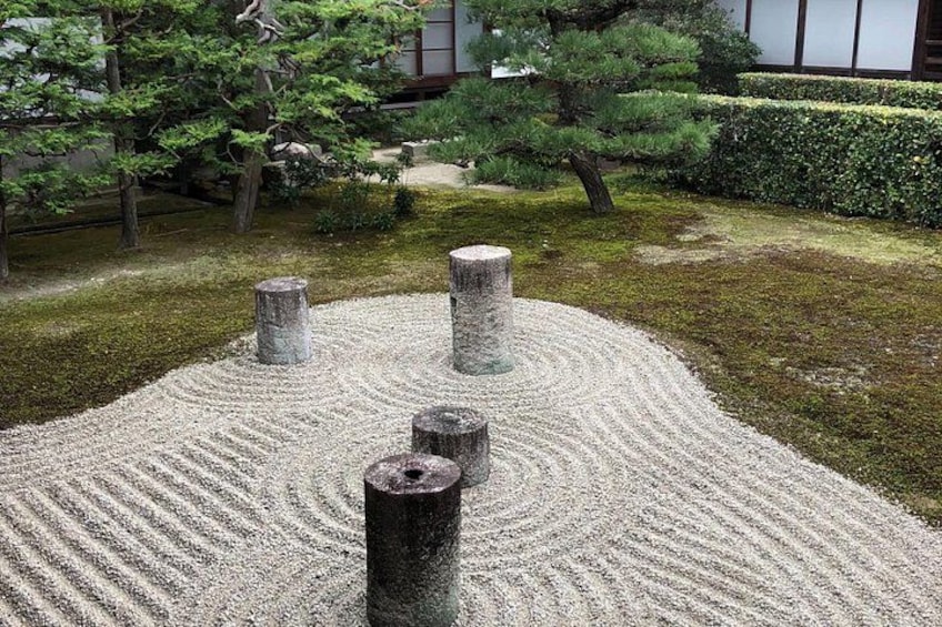 A Zen garden with raked gravel, stone lanterns, and a pine tree. 5