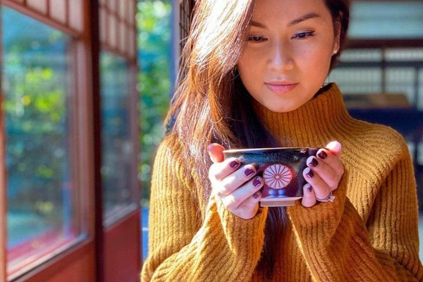 A person holding a mug with a design, wearing a yellow sweater, standing indoors near a window. 1
