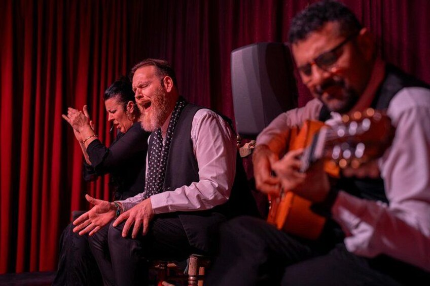 En scene med tre personer, hvoraf den ene spiller guitar og de to andre samtaler. 3