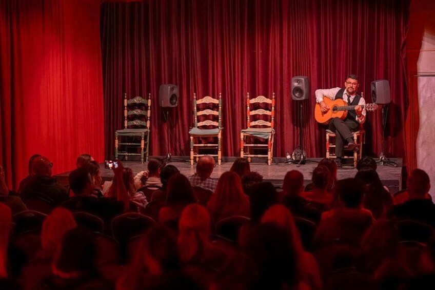 Un palco con un uomo che suona la chitarra, tende rosse e sedie. 2