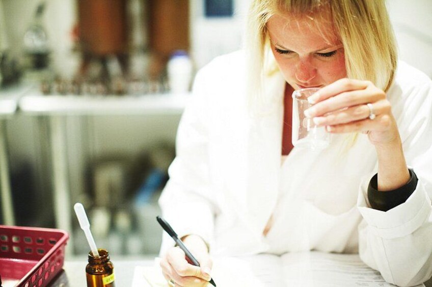 Une personne vêtue d’une blouse de laboratoire blanche, assise à une table et écrivant avec un stylo, un verre d’eau à portée de main. 2