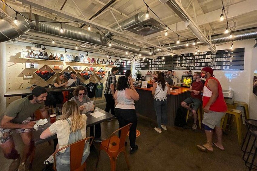 Un bar con gente sentada y de pie, una barra con bebidas y estantes con botellas. 2