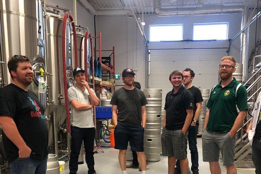 Un grupo de personas en una cervecería, con tanques de acero inoxidable y equipo de elaboración. 1