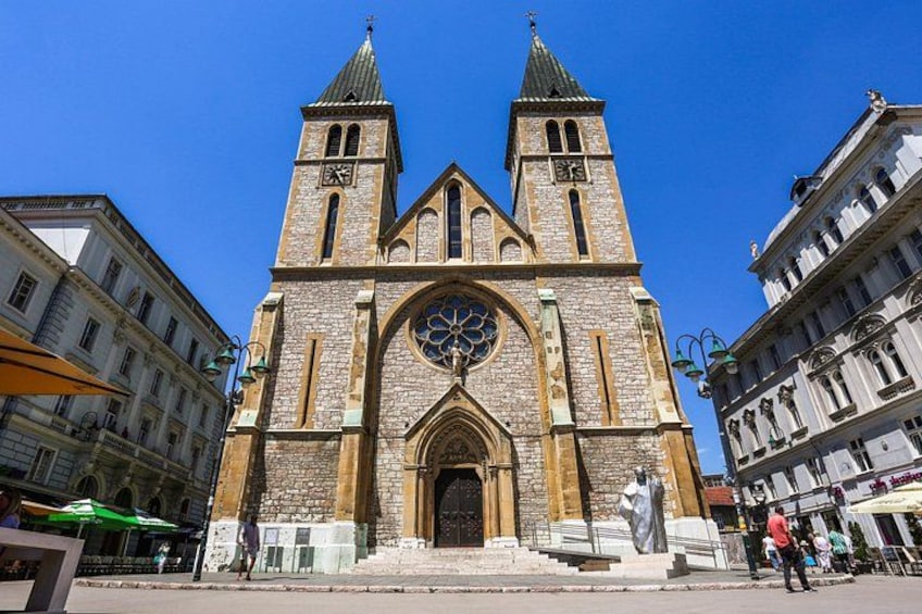 A historic church with two towers, a large clock, and a statue in front. 5