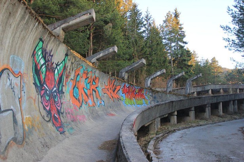 A concrete structure with graffiti, a curved road, and trees in the background. 4