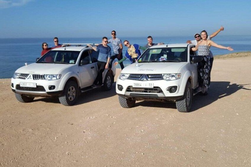 Two white SUVs parked on a beach with people standing around them. 4