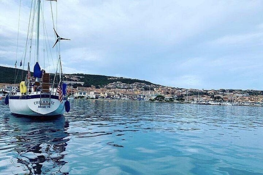 Un velero llamado 'CHICKEN FLY' anclado cerca de un pueblo costero con edificios al fondo. 3