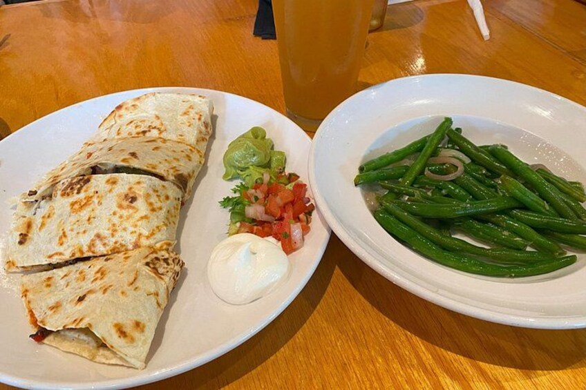 Une assiette comprenant un burrito, de la guacamole, de la crème aigre et une portion de haricots verts. 2