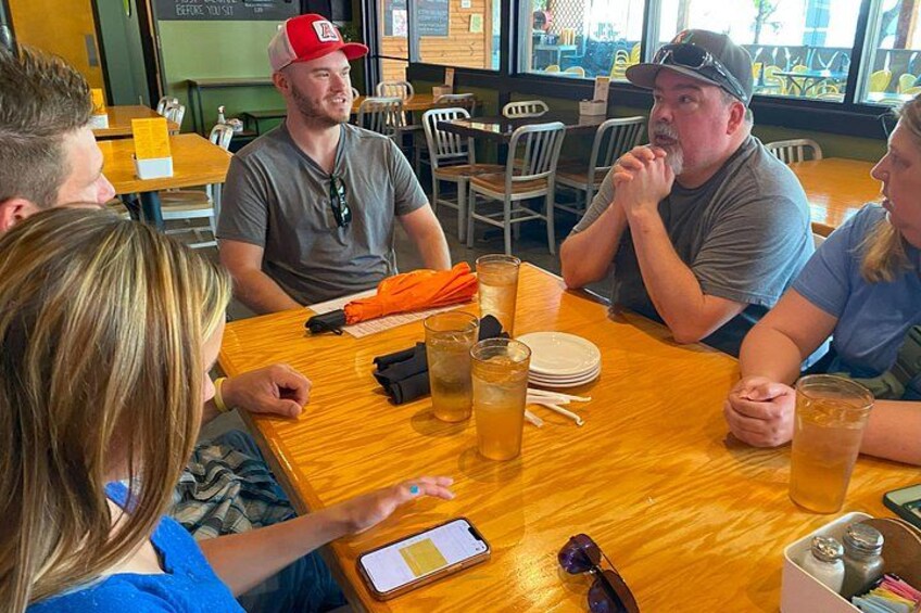 Un groupe de personnes est assis autour d’une table en bois dans un restaurant, avec des boissons et un menu devant eux. 3