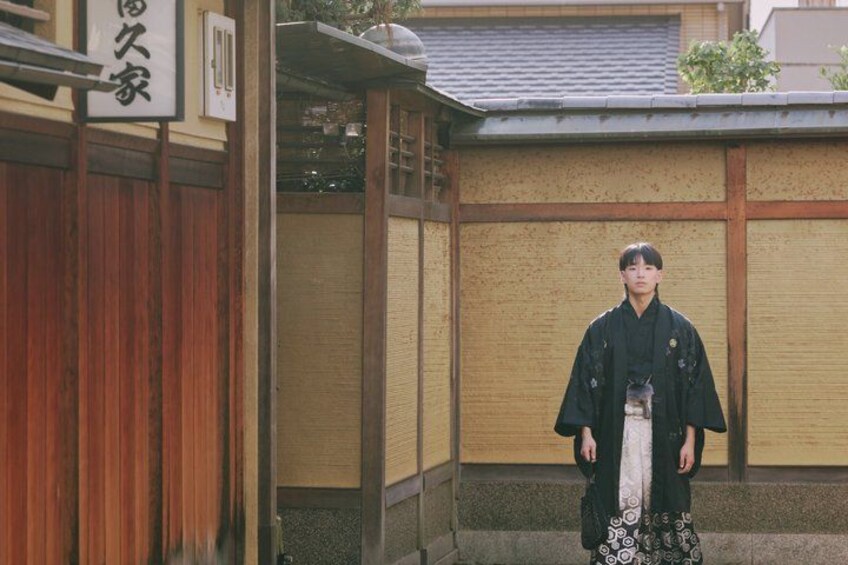 En person i traditionelt japansk tøj står foran en bygning med træfacade og et skilt med japanske tegn. 2