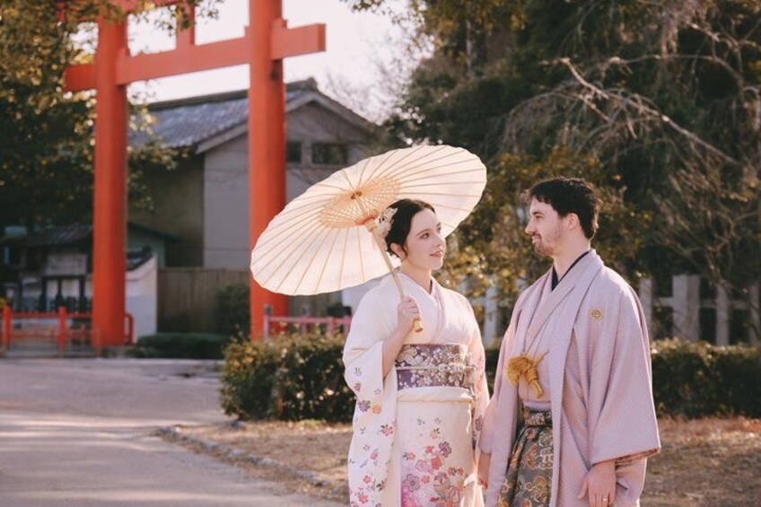 Et par iført traditionelt japansk tøj står foran en rød torii-port. 1