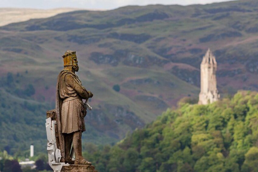 Una estatua de una figura histórica domina un paisaje con una torre destacada al fondo. 3
