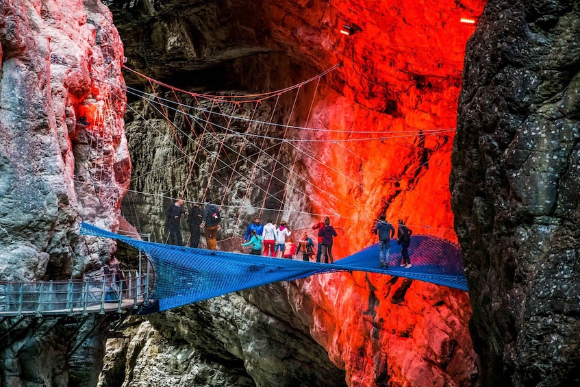 A rope bridge over a red-lit cave with people walking across. 4