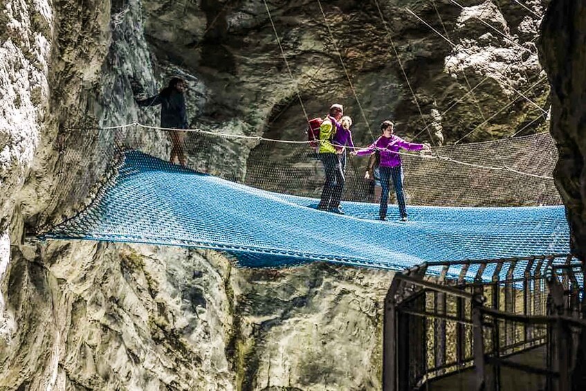 People crossing a rope bridge in a rocky canyon. 1